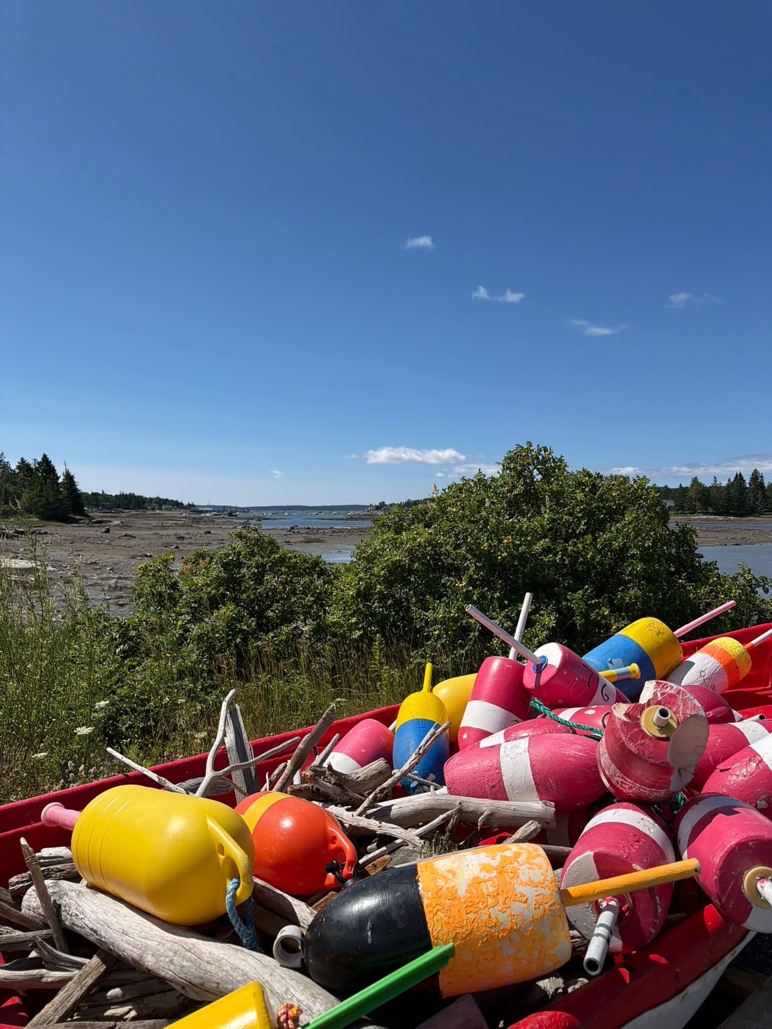 Colorful lobster buoys and driftwood piled in a red boat overlooking the rocky shoreline and water of Bass Harbor, Maine.