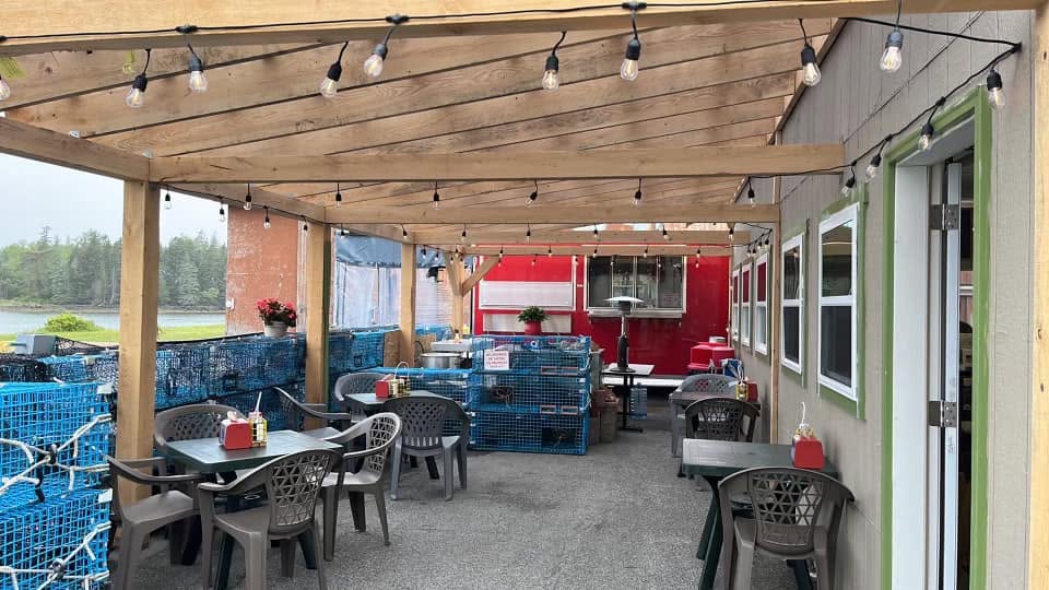 Covered outdoor dining area at Archie’s Lobster with picnic-style tables, string lights, lobster traps, and waterfront views.