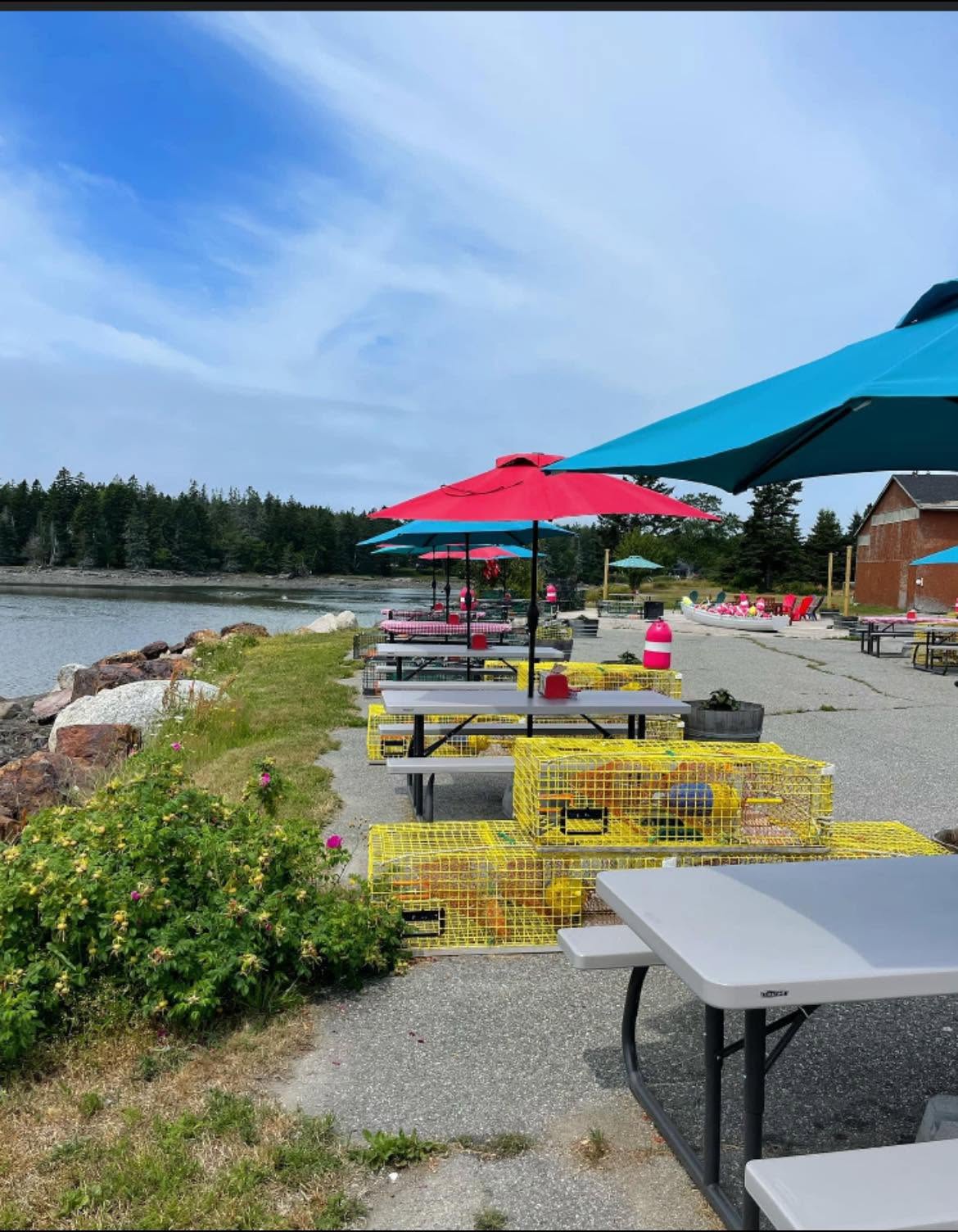 Outdoor picnic tables with colorful umbrellas beside the water at Archie’s Lobster in Bass Harbor, Maine.